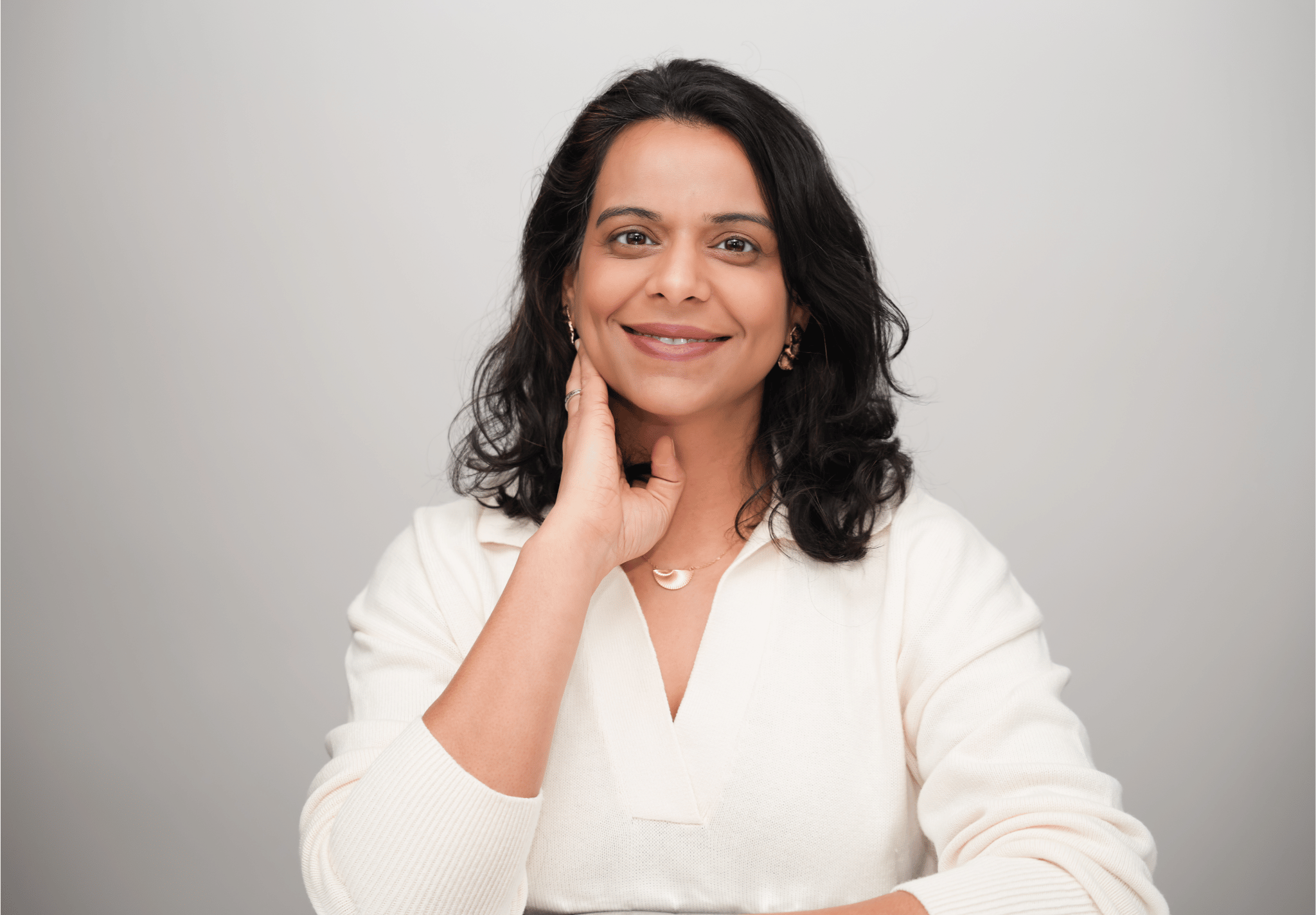 Woman in a white shirt posing with one hand on her chin against a light gray background